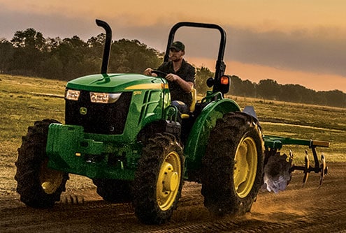 Farmer driving the compact utility tractor with an attachment.