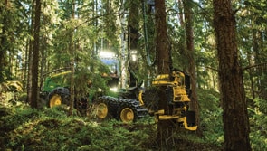 John Deere harvester removing tree trunk in forest