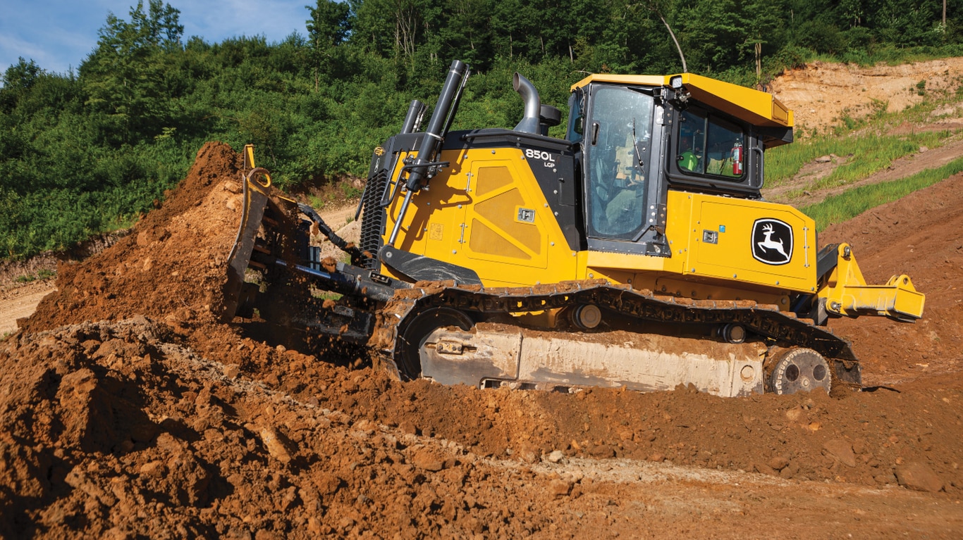 850L Dozer pushing dirt on unlevel terrain with trees in the background.