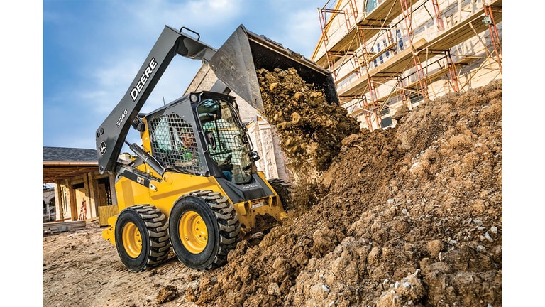 A 324G Skid Steer dumping dirt and rocks at a worksite.