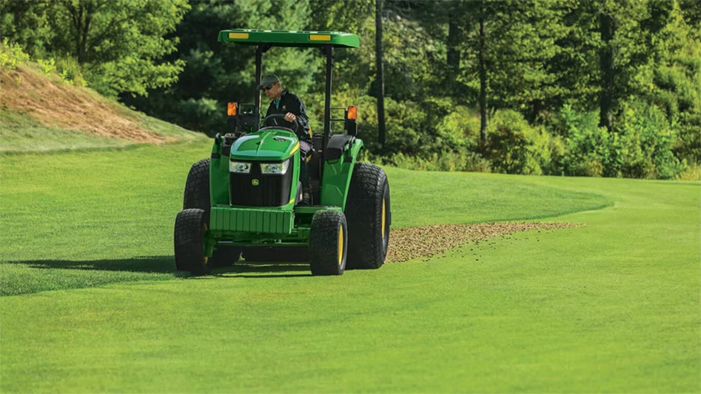 Worker driving a 4066M utility tractor on grass for property maintenance and farm work.