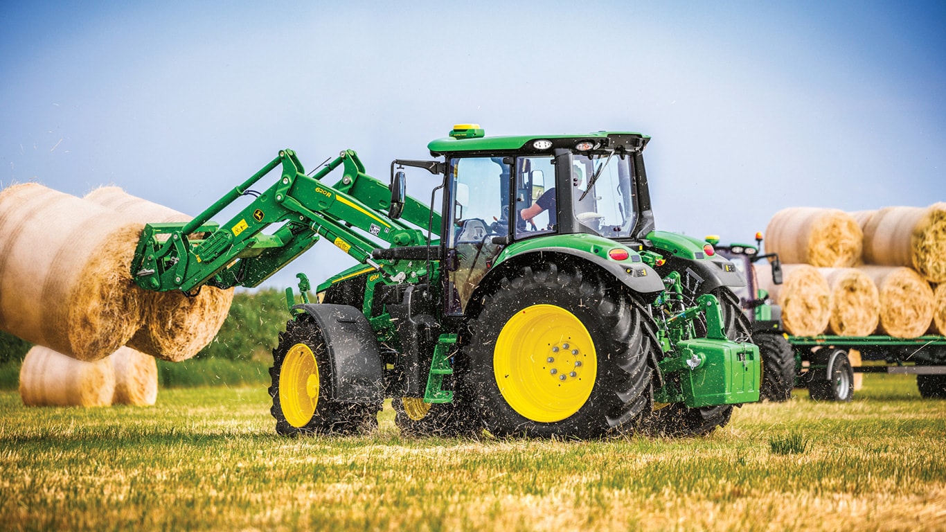 6M with loader picking up hay bales