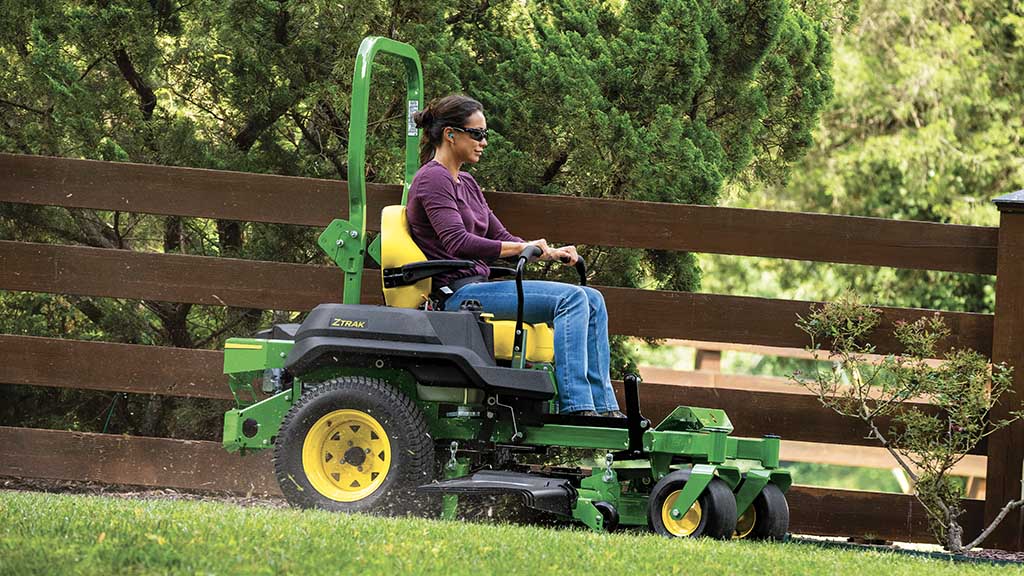 Image of a woman riding a zero-turn mower in a fenced yard.