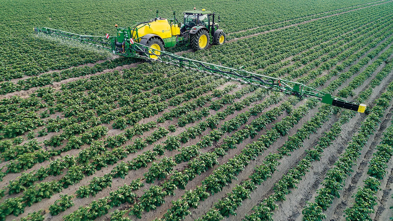 tractor pulling a green and yellow sprayer through a field of crops