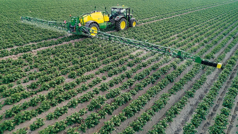tractor pulling a green and yellow sprayer through a field of crops