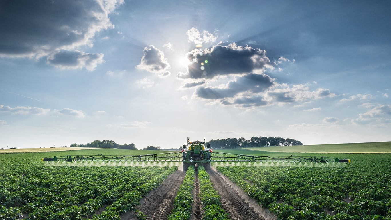 head on view of a tractor pulling a sprayer through a field of crops
