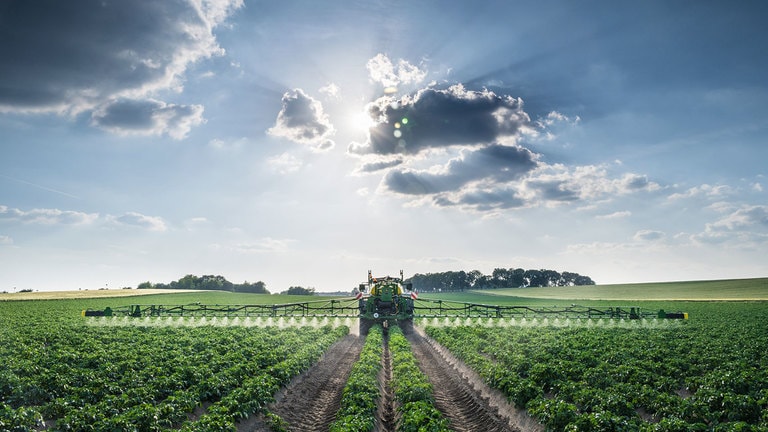 head on view of a tractor pulling a sprayer through a field of crops
