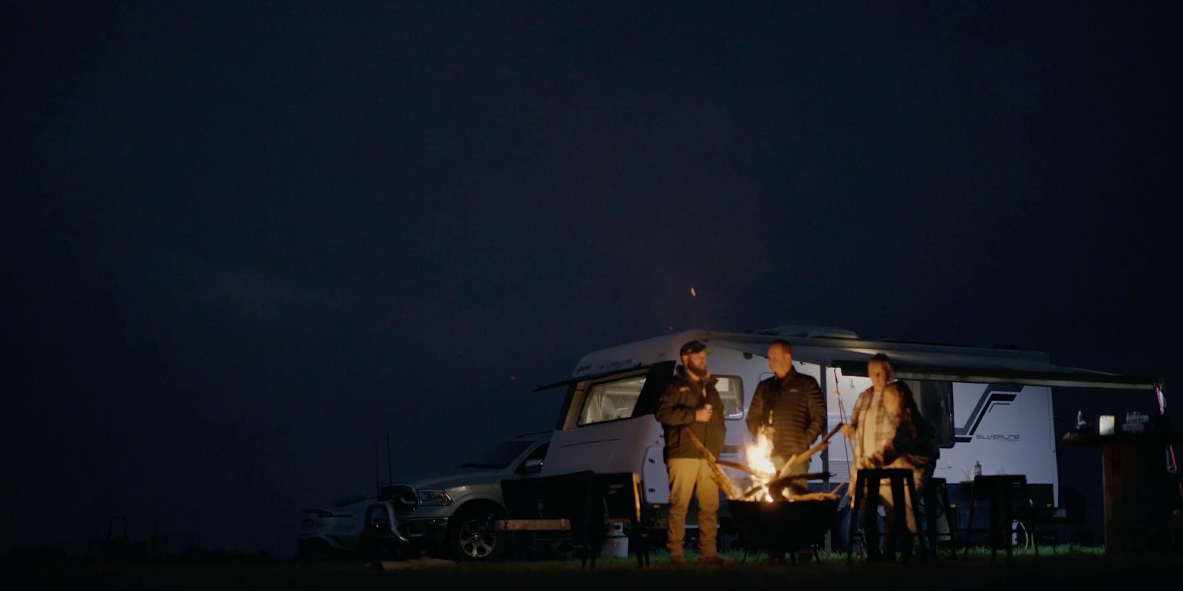 The Furners standing by a campfire next to their caravan on clear, starry night