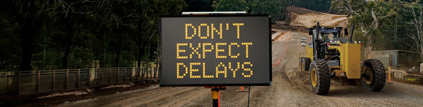 Expect delays lighted sign in road construction zone with a grader.