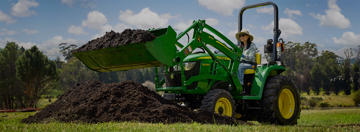 Woman using a Deere Compact Tractor for work on her land
