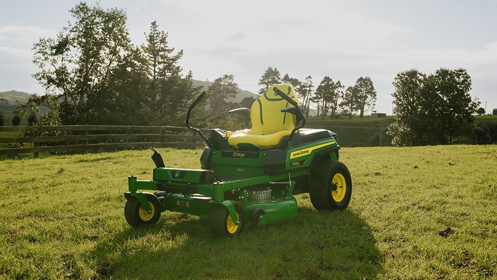 John Deere ZTrak green and yellow lawn mower on grass with trees in the background.