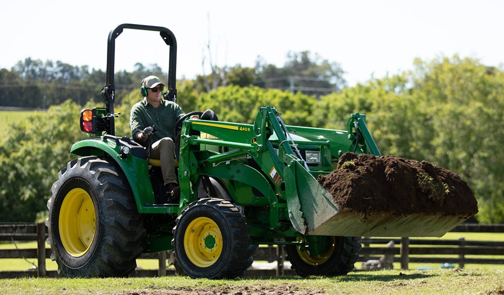 A person moving dirt with a John Deere 4044R Compact Utility Tractor.