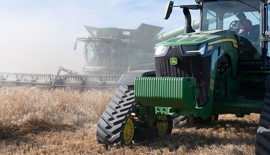 A John Deere tractor and Combine Harvester are working in tandem in a field.