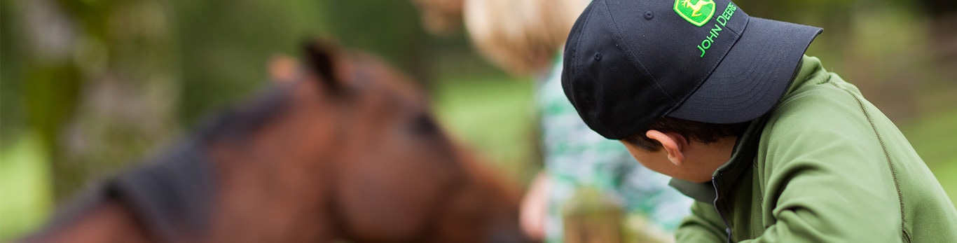 young boy looking sideways at brown horse in a barn