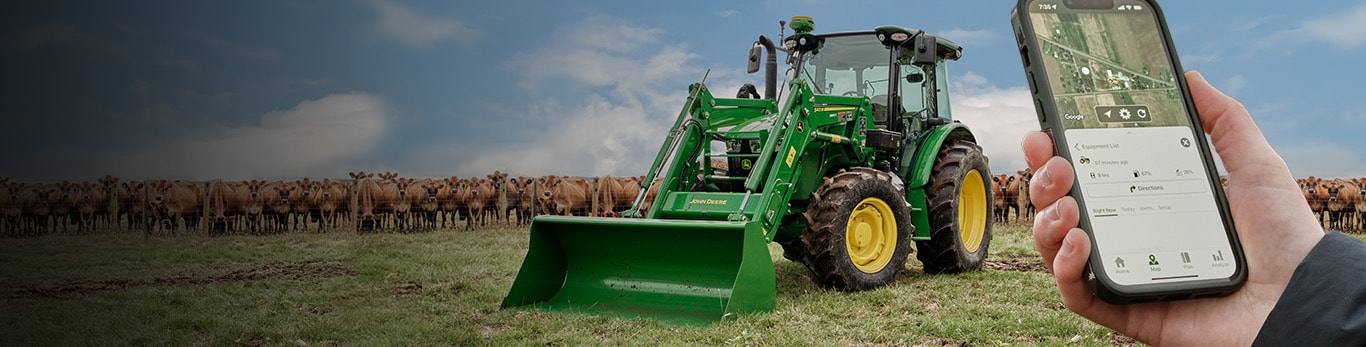 Tractor with 543M loader in front of a fence with cows behind it and a hand holding their phone tracking the tractor.