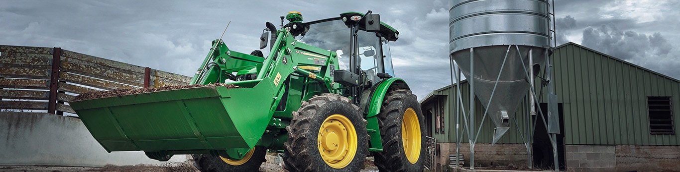 Tractor with loader in front of fence and farm equipment