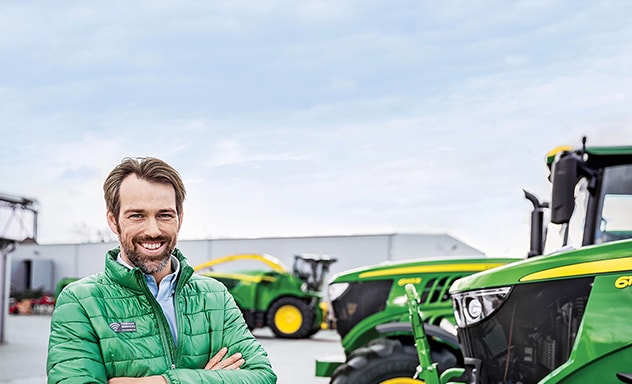 Man with arms crossed standing to the left of tractor