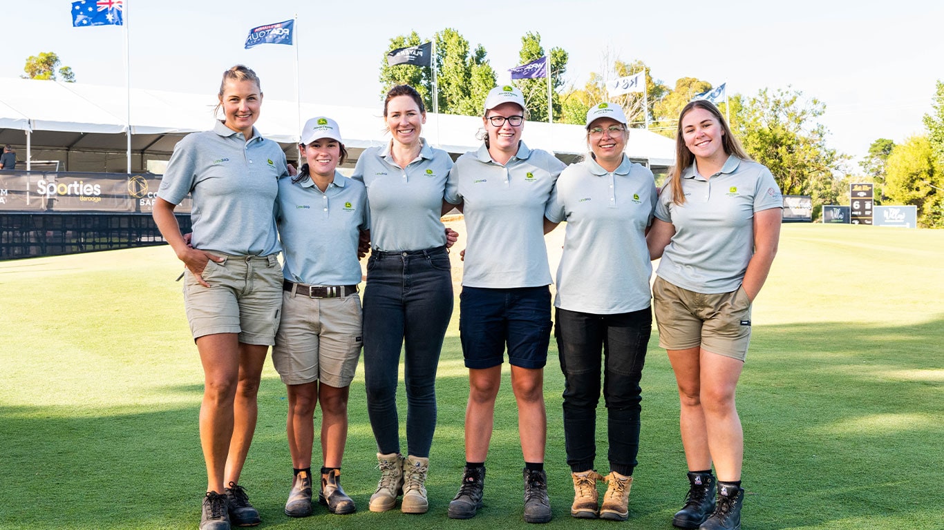 The six female greenskeepers standing on the golfing green smiling.