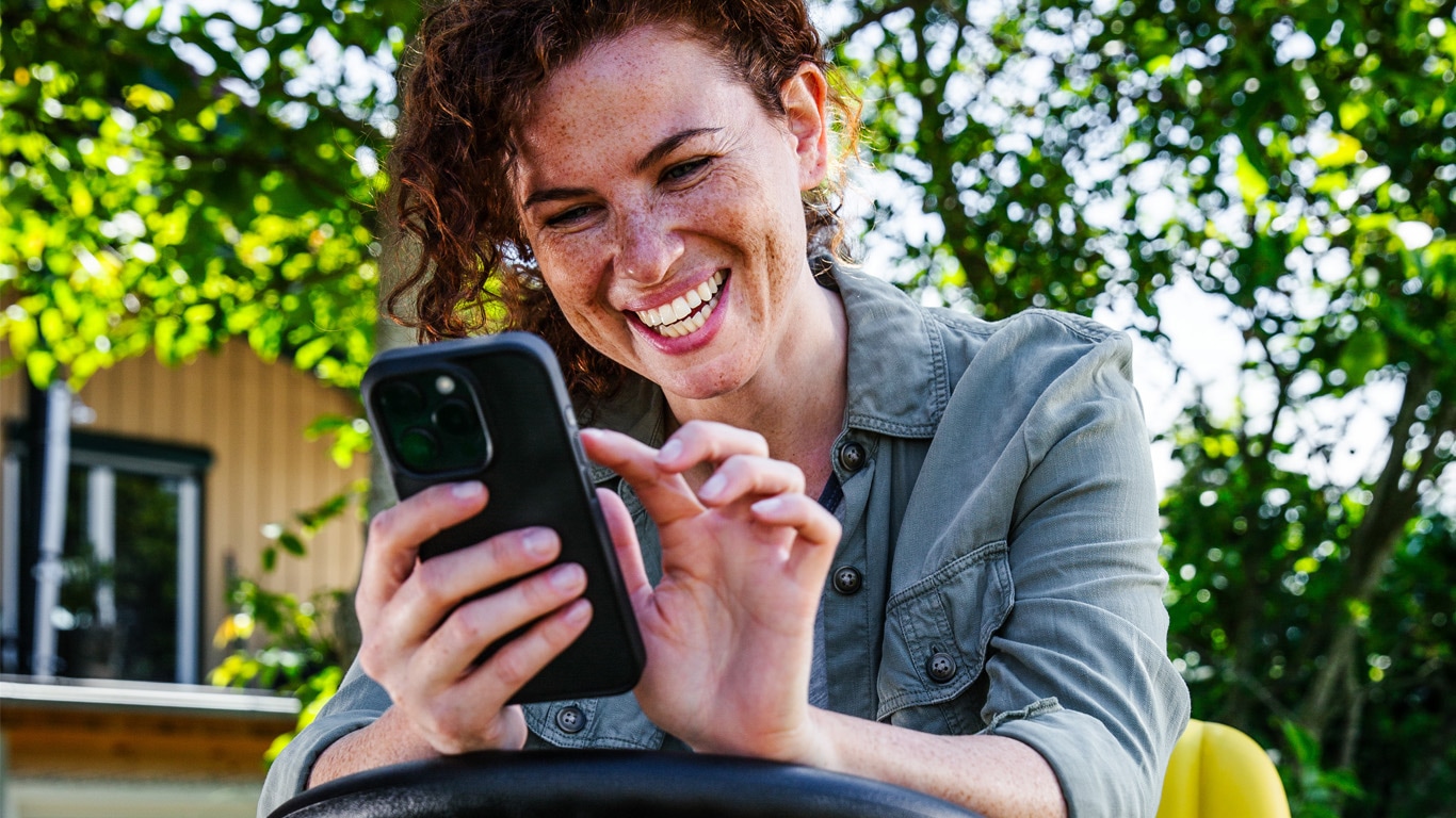 Woman sitting on riding lawn equipment smiling and looking at phone in her hand