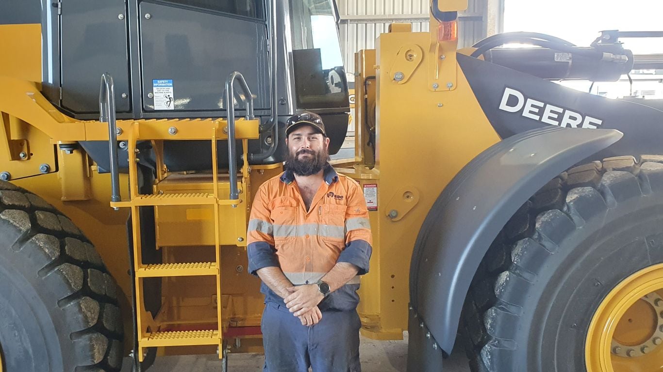 A man wearing an orange high visibility shirt standing next to a large green forestry machine.