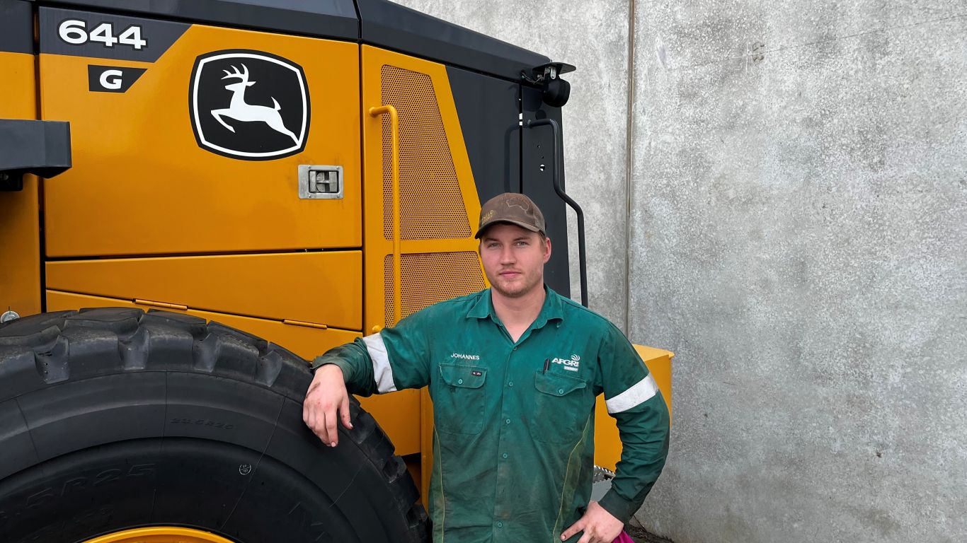 A man wearing a dark green shirt standing next to a large yellow construction machine.