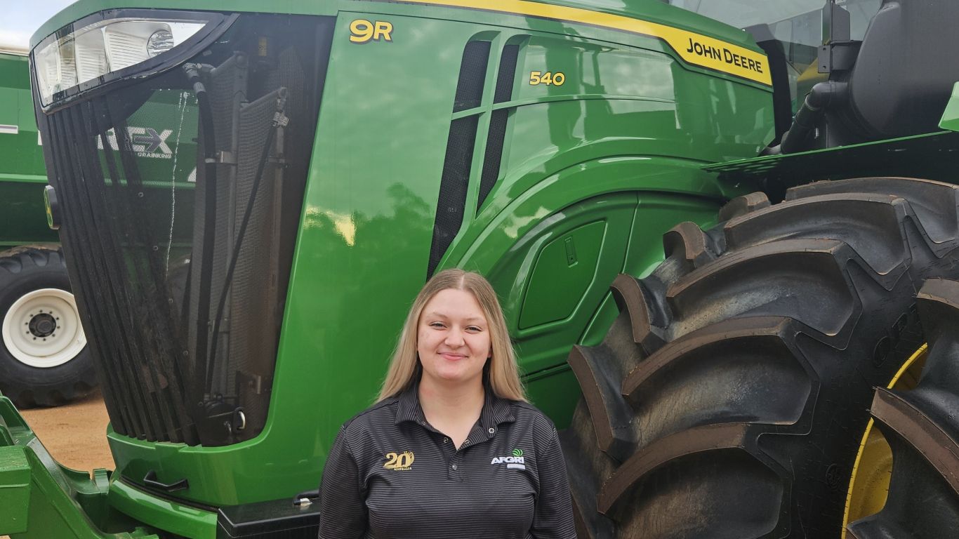 A lady wearing a black polo shirt standing in front of a large green tractor.