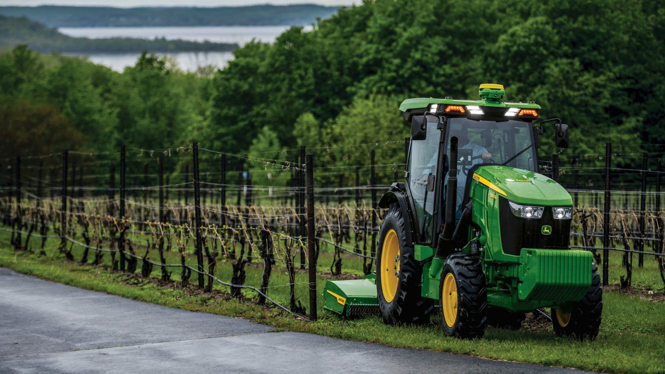 A Deere tractor works in a vineyard, surrounded by lush greenery.