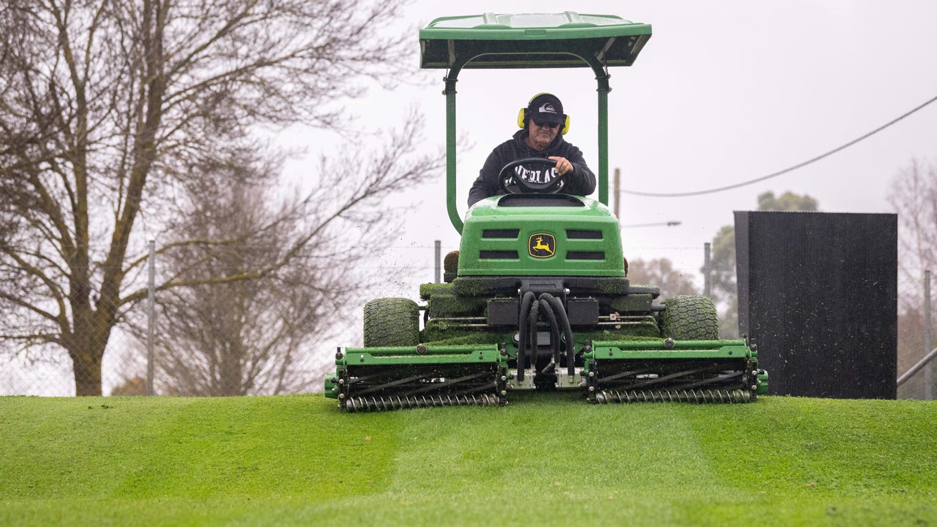 Man driving ride on mower on green.