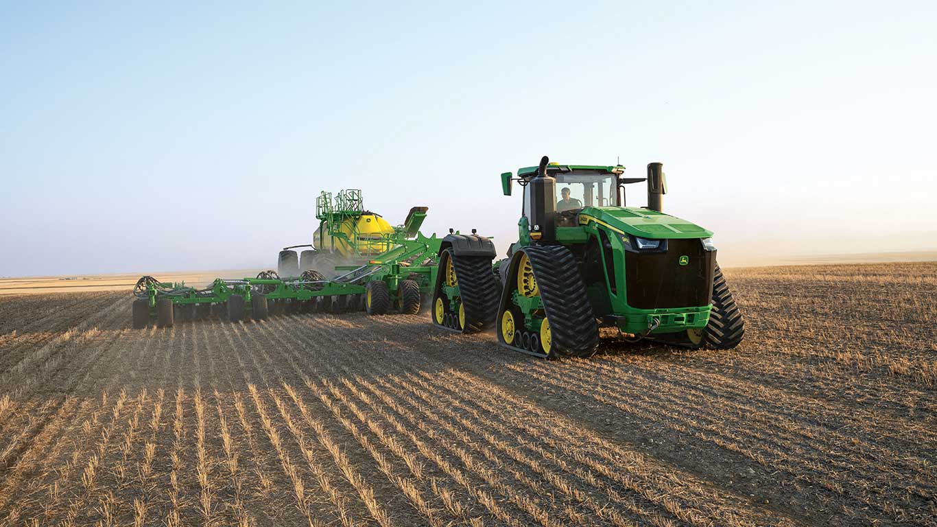John Deere tractor with seeding equipment in a field at sunset