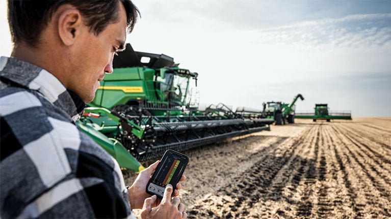 farmer using Connect Mobile in field with John Deere combine fleet