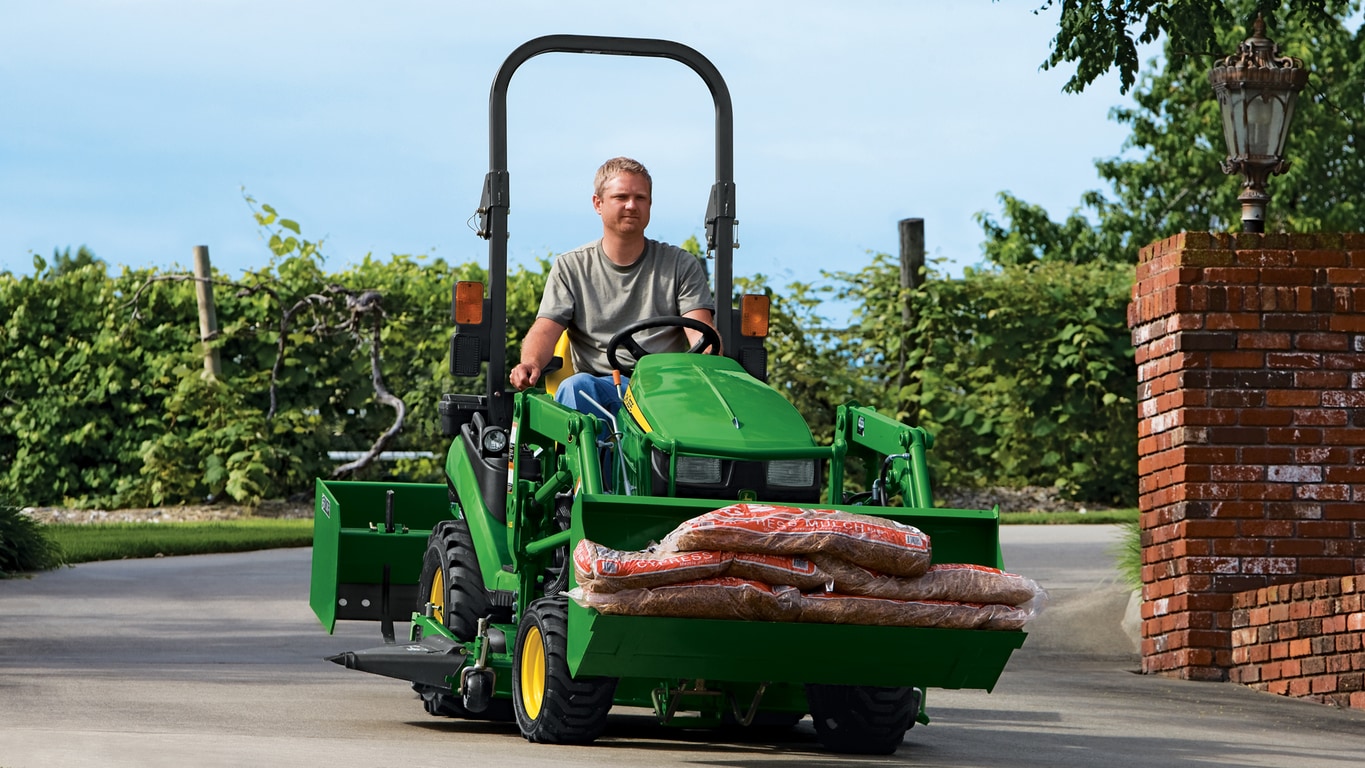 Man driving small John Deere tractor with attachments and implements