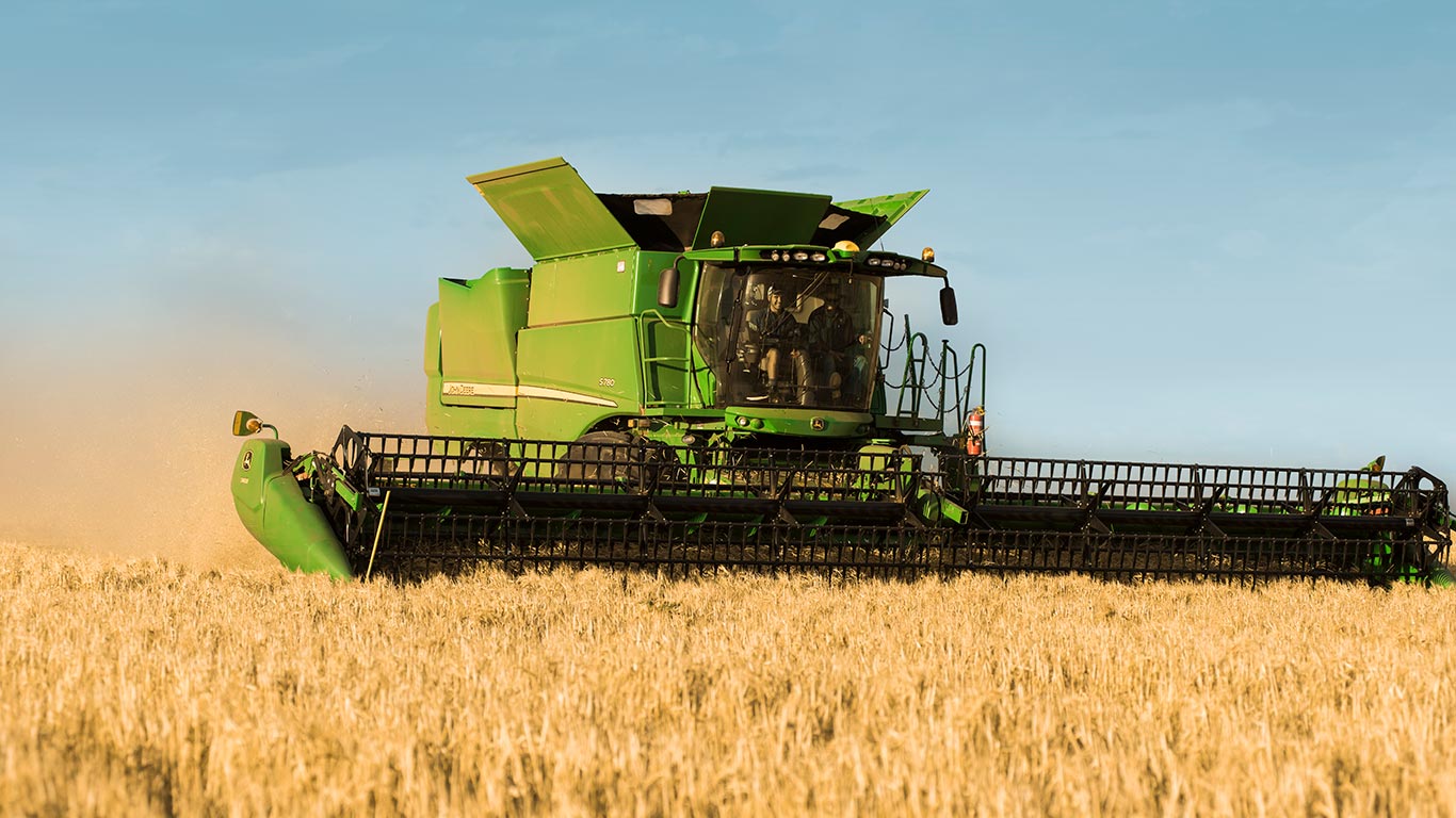 Photo of a John Deere S7 Combine with a corn head, completing a pass in corn