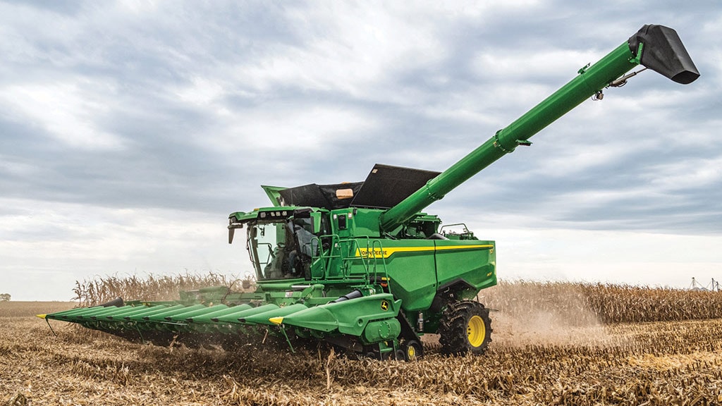 Combine harvester harvesting corn in a field under a cloudy sky, creating dust as it moves along the rows of crops. Combine harvester harvesting corn in a field under a cloudy sky, creating dust as it moves along the rows of crops.