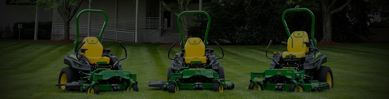 Three green zero-turn mowers resting on a well-kept stripped lawn.
