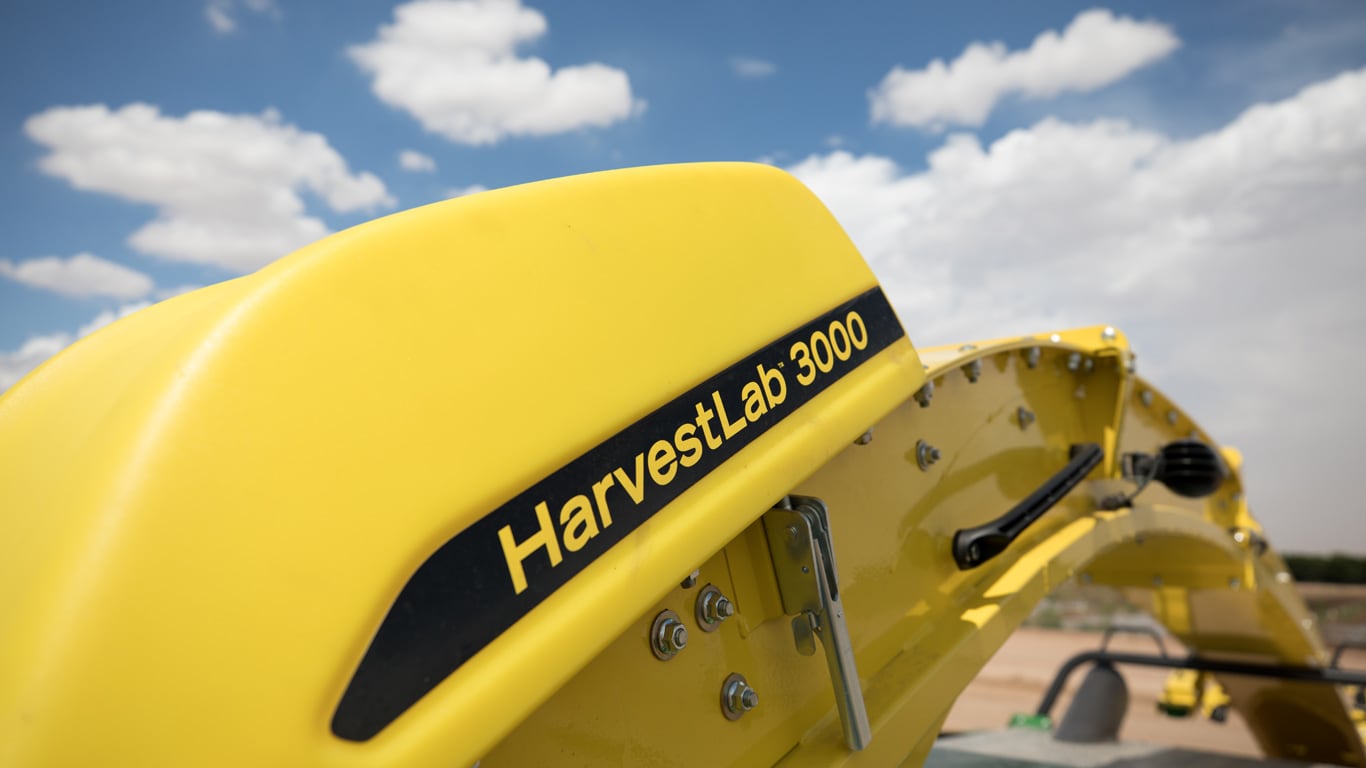Yellow 'HarvestLab 3000' machine close-up under blue sky with scattered white clouds.