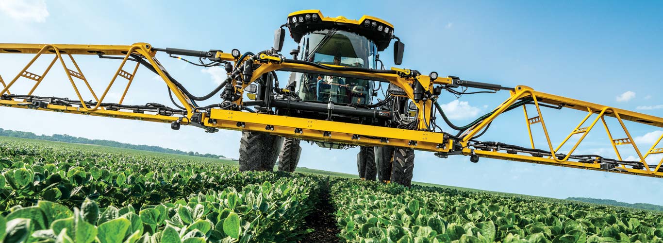 Hagie sprayer with front-mounted hybrid boom in field.