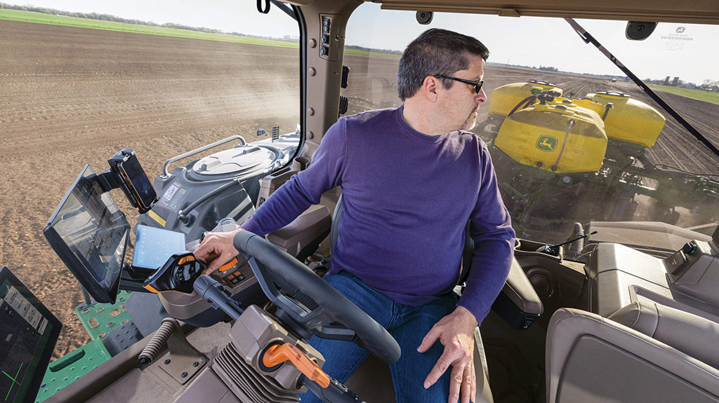 Operator in cab swiveled in his seat looking back at a planter while operating a high-horsepower 8 Series Tractor.