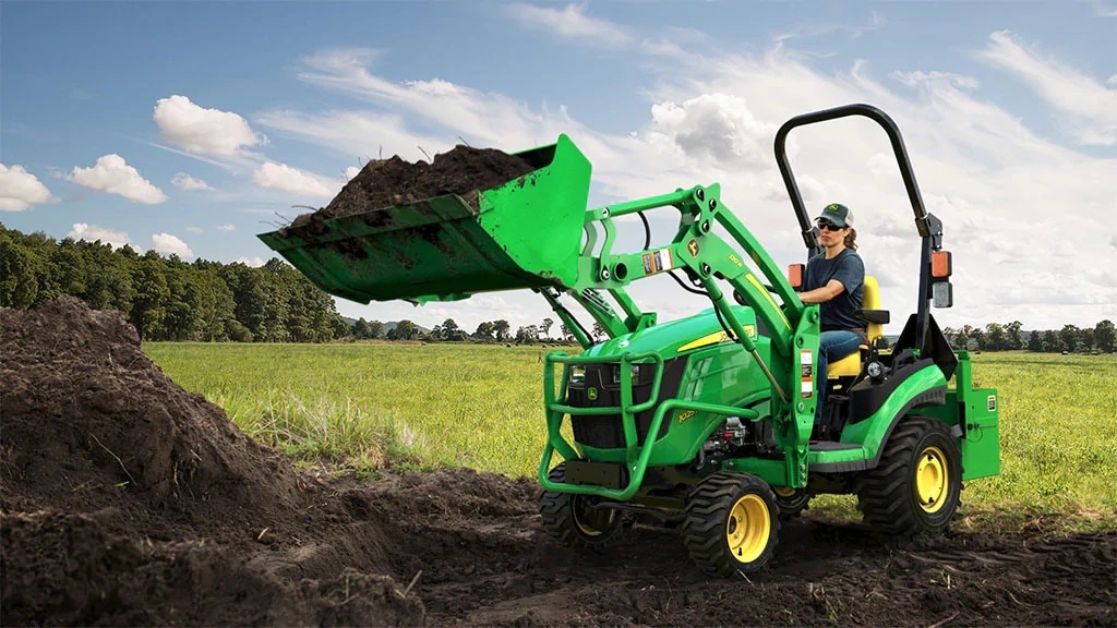 Woman driving small John Deere tractor with attachments and implements