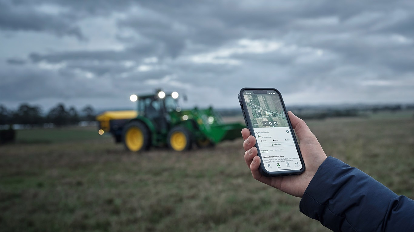 person holding up a phone with JD Link displayed, a tractor is in a field in the background